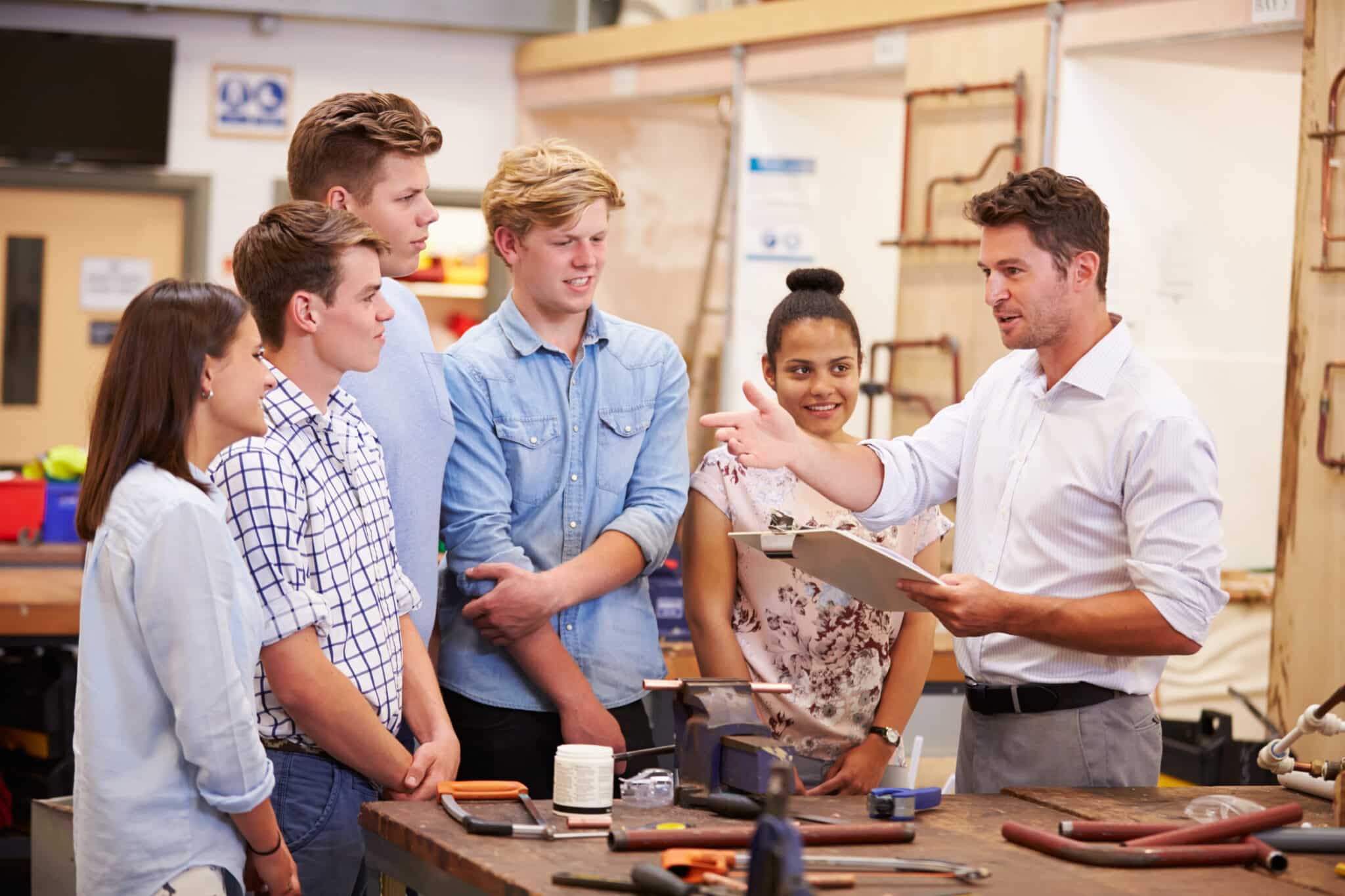 Studium und Ausbildung: Lehrer hilft Schülern in einer Werkstatt